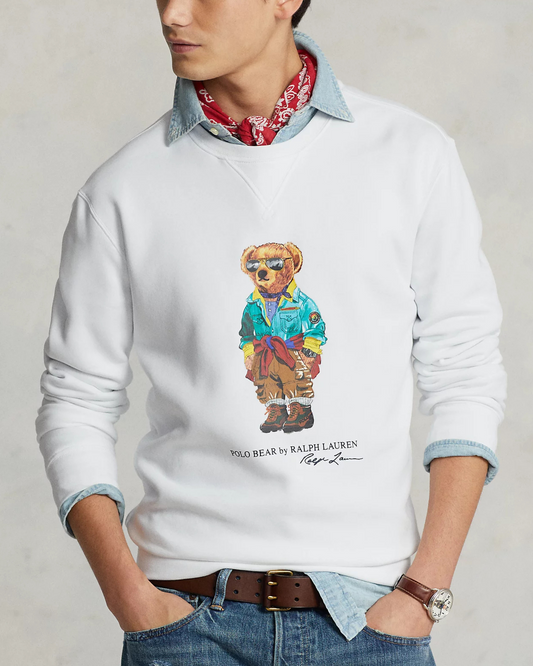 A male model wearing a white Polo Ralph Lauren Bear Crew Jumper, featuring a colorful embroidered bear graphic on the chest. Styled with a denim shirt underneath and a red bandana around the neck